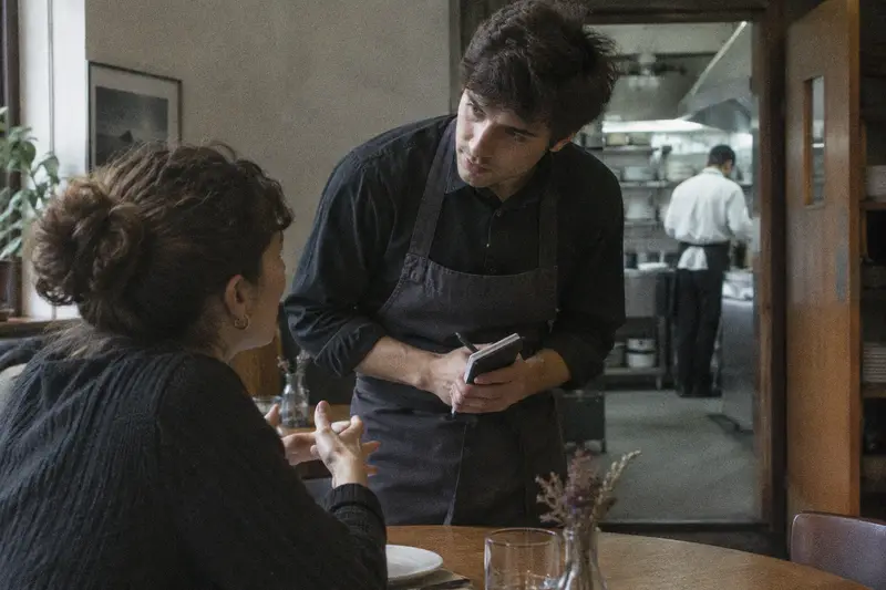 Un camarero escucha a una clienta que le explica su alergia en la mesa de un restaurante