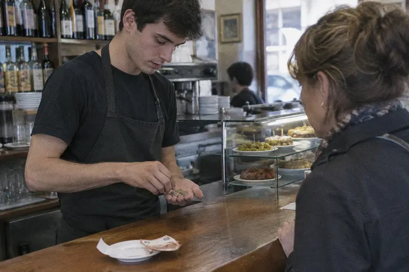 Un camarero cuenta el cambio en la mano delante de una clienta en la barra de un bar de tapas