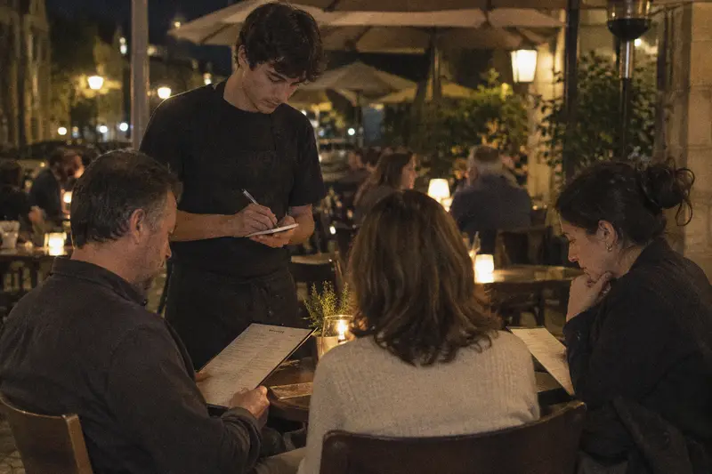 Un camarero toma nota con su libreta en una mesa de terraza con tres clientes