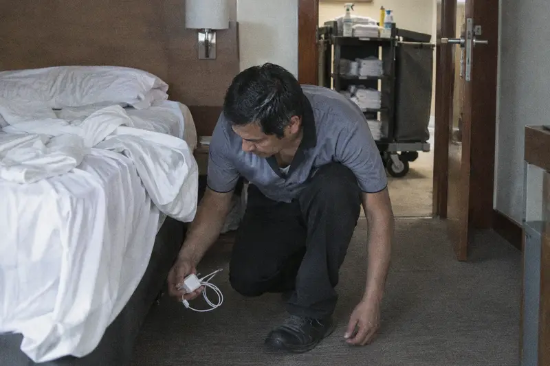 Un camarero de pisos sostiene un cargador de móvil que ha encontrado debajo de la cama de una habitación de hotel