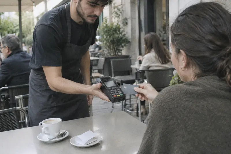 Un cliente paga con tarjeta en el datáfono que le acerca el camarero en una terraza