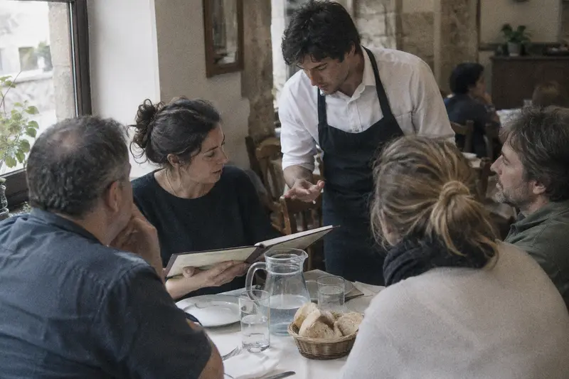 Un camarero explica la carta a cuatro turistas sentados a la mesa