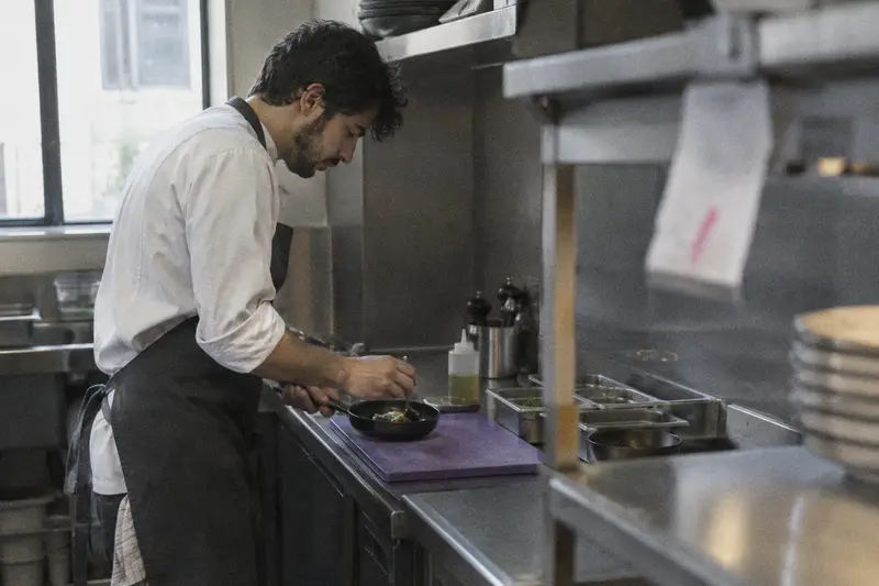 Un cocinero prepara un plato aparte con una tabla morada y una sartén limpia