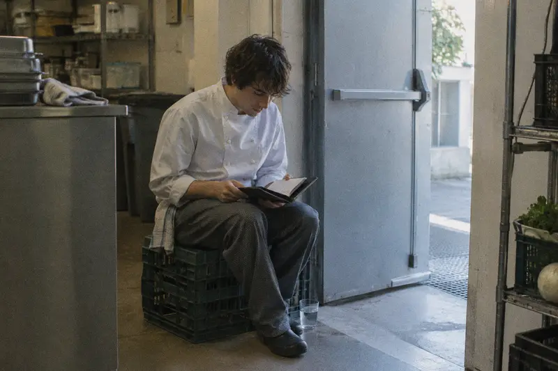Un cocinero repasa sus notas en una libreta durante el descanso junto a la puerta de la cocina