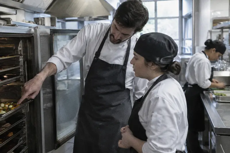 Un jefe de cocina explica una tarea a una cocinera nueva junto a la cámara abierta