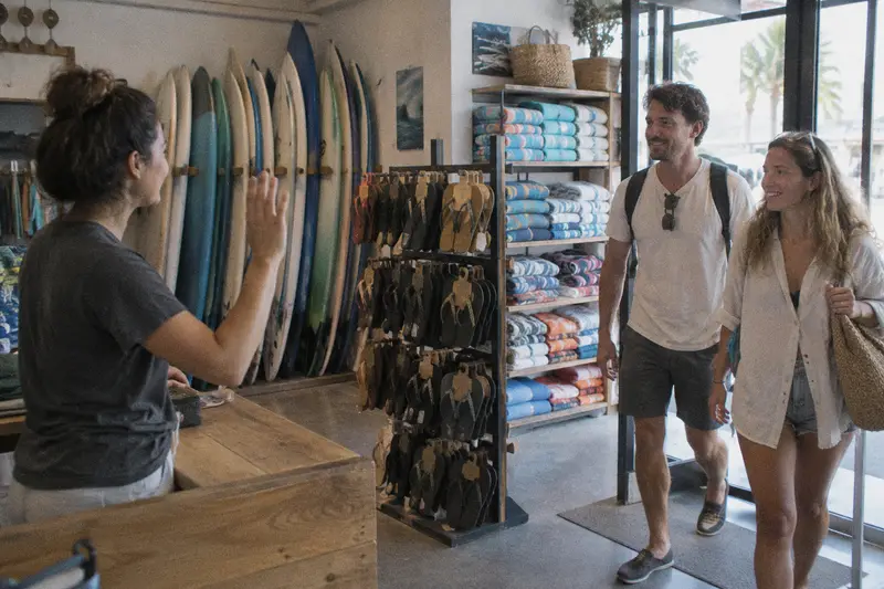 Una dependienta saluda a una pareja de turistas que entra en una tienda de surf