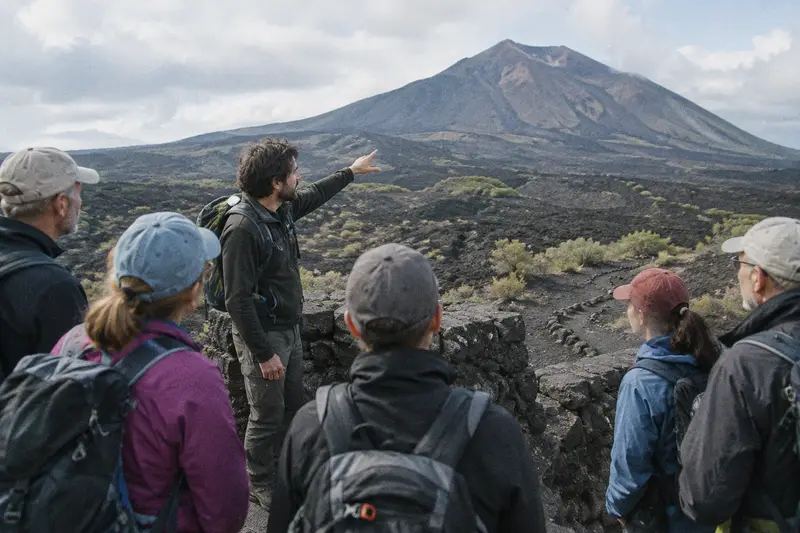 Un guía señala un volcán a un grupo de senderistas desde un mirador en un paisaje de lava
