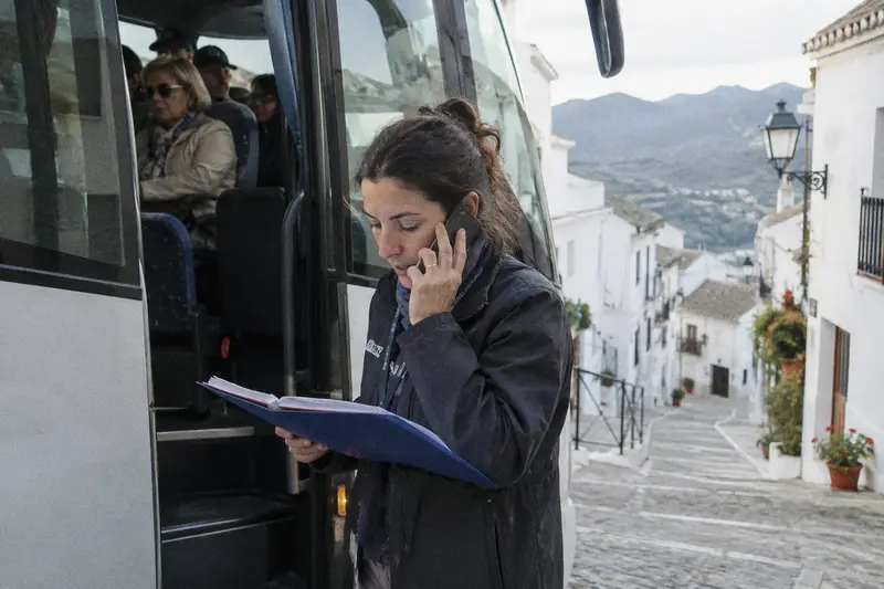 Una guía turística habla por el móvil junto a la puerta de un autobús mientras el grupo espera dentro