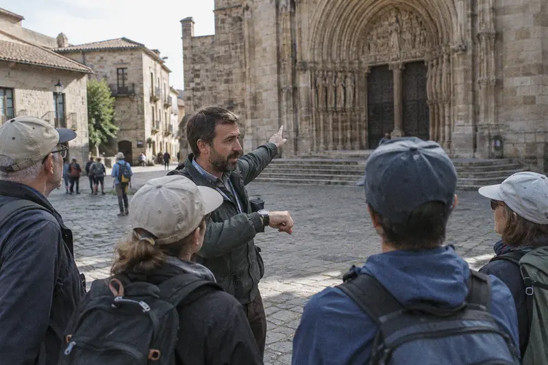 Un guía turístico señala la puerta de una catedral y enseña su reloj a un grupo de turistas en una plaza