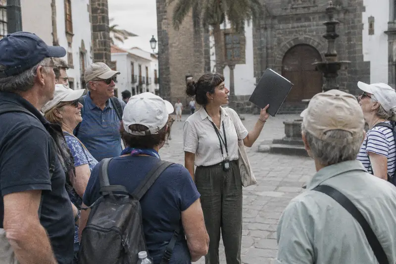 Una guía con una carpeta levantada da la bienvenida a un grupo de turistas en una plaza por la mañana
