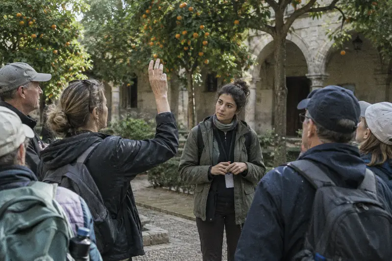 Una guía turística escucha la pregunta de una turista en un patio con naranjos mientras el grupo espera