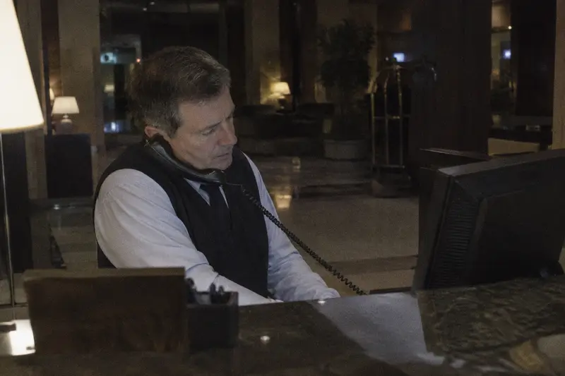 Un recepcionista habla por el teléfono del mostrador de un hotel de noche con el vestíbulo vacío detrás