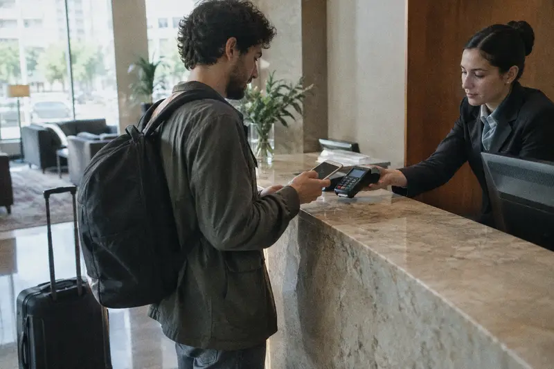 Un huésped paga con el móvil en el datáfono que le acerca la recepcionista al dejar el hotel