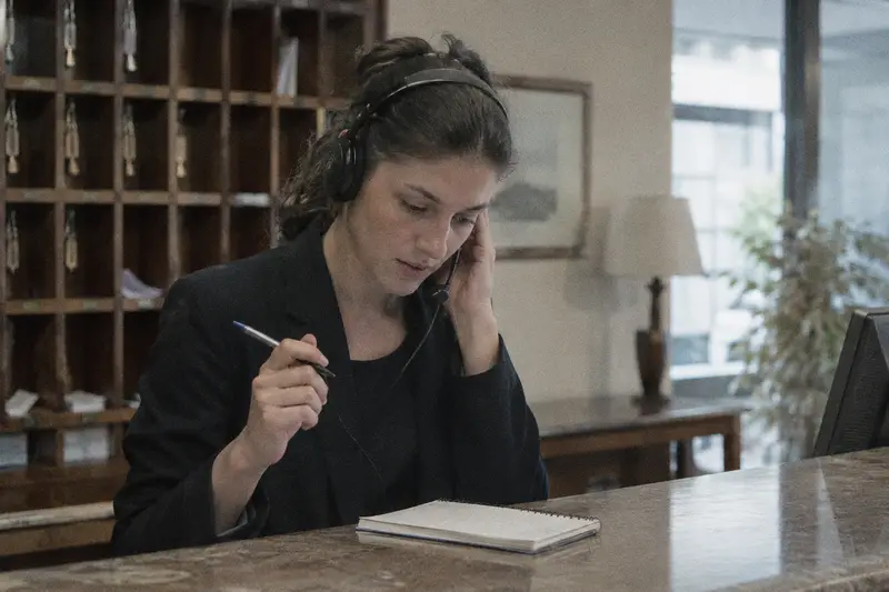Una recepcionista con cascos apunta en un bloc mientras escucha a un cliente por teléfono