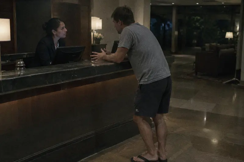 Una recepcionista escucha con atención la queja de un huésped en el mostrador del hotel por la noche