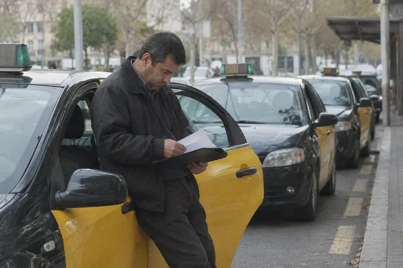 Un taxista repasa unas hojas apoyado en su coche mientras espera en la parada de taxis