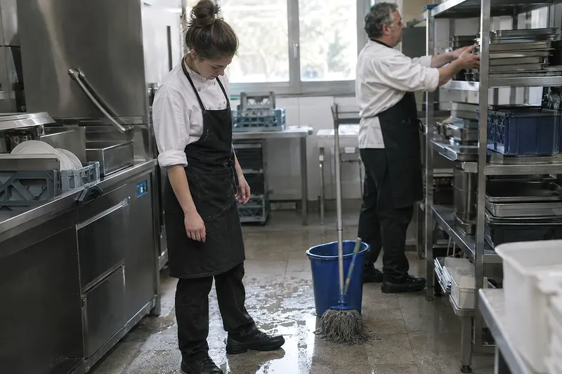 Una cocinera joven mira el suelo mojado junto al lavavajillas de una cocina de hotel