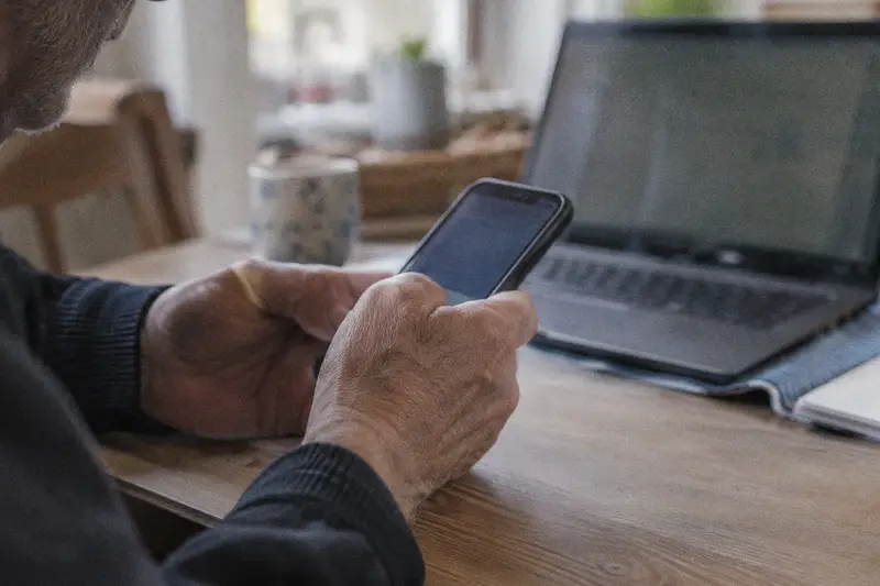 Las manos de un hombre mayor con el móvil para entrar en una web oficial desde casa