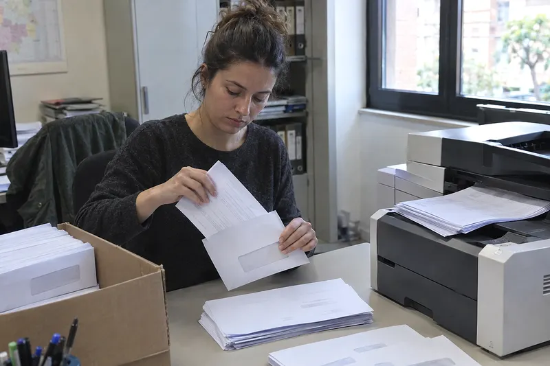 Una auxiliar mete cartas impresas en sobres con ventana junto a la impresora de la oficina