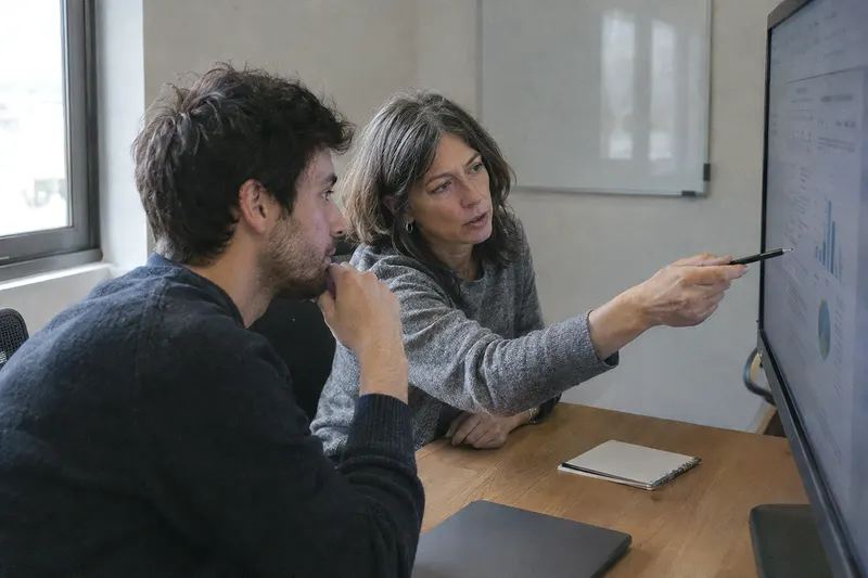 Dos compañeros revisan juntos un documento en el monitor de una sala de reuniones